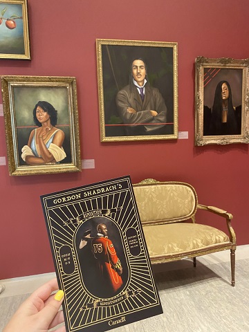 Trois portraits suspendus et une main tenant un dépliant de l'exposition