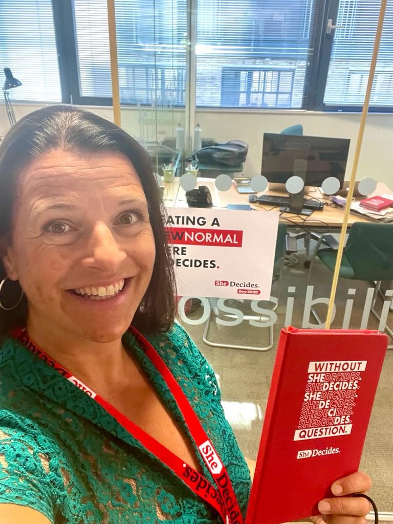 Karin Nilsson wearing a green shirt and a red SheDecides lanyard holds a red book entitled Without Question. SheDecides