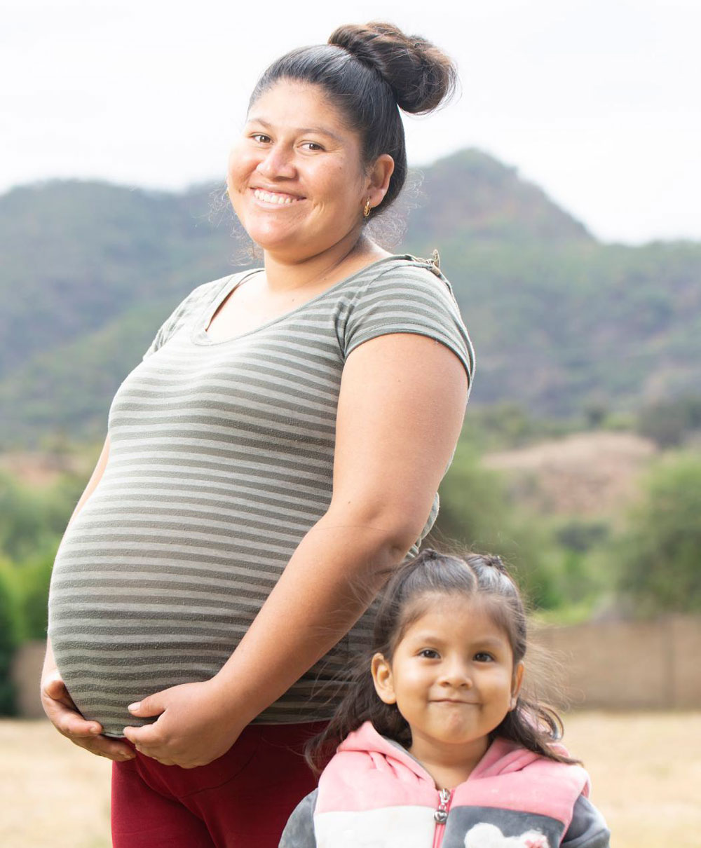 A pregnant woman and toddler smile at the camera.